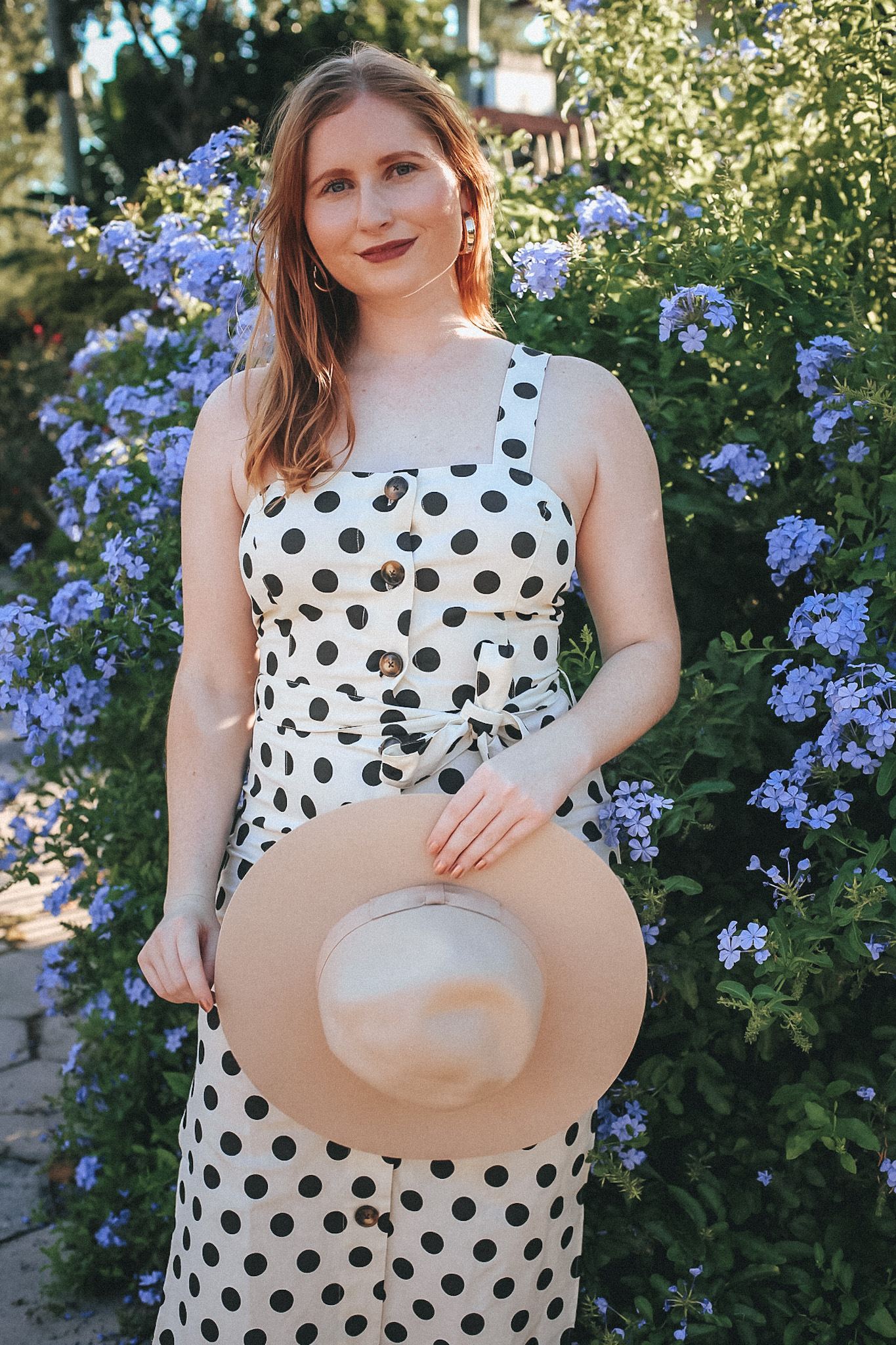 A Budget-Friendly Everyday Dress. Florida style blogger Amanda Burrows of the fashion blog Affordable by Amanda shares her favorite Spring Dresses Under $50. Amanda wears a casual JustFab Belted Button Front Dress with polka dot print. She is also holding a felt Urban Outfitters wide-brim beige hat.