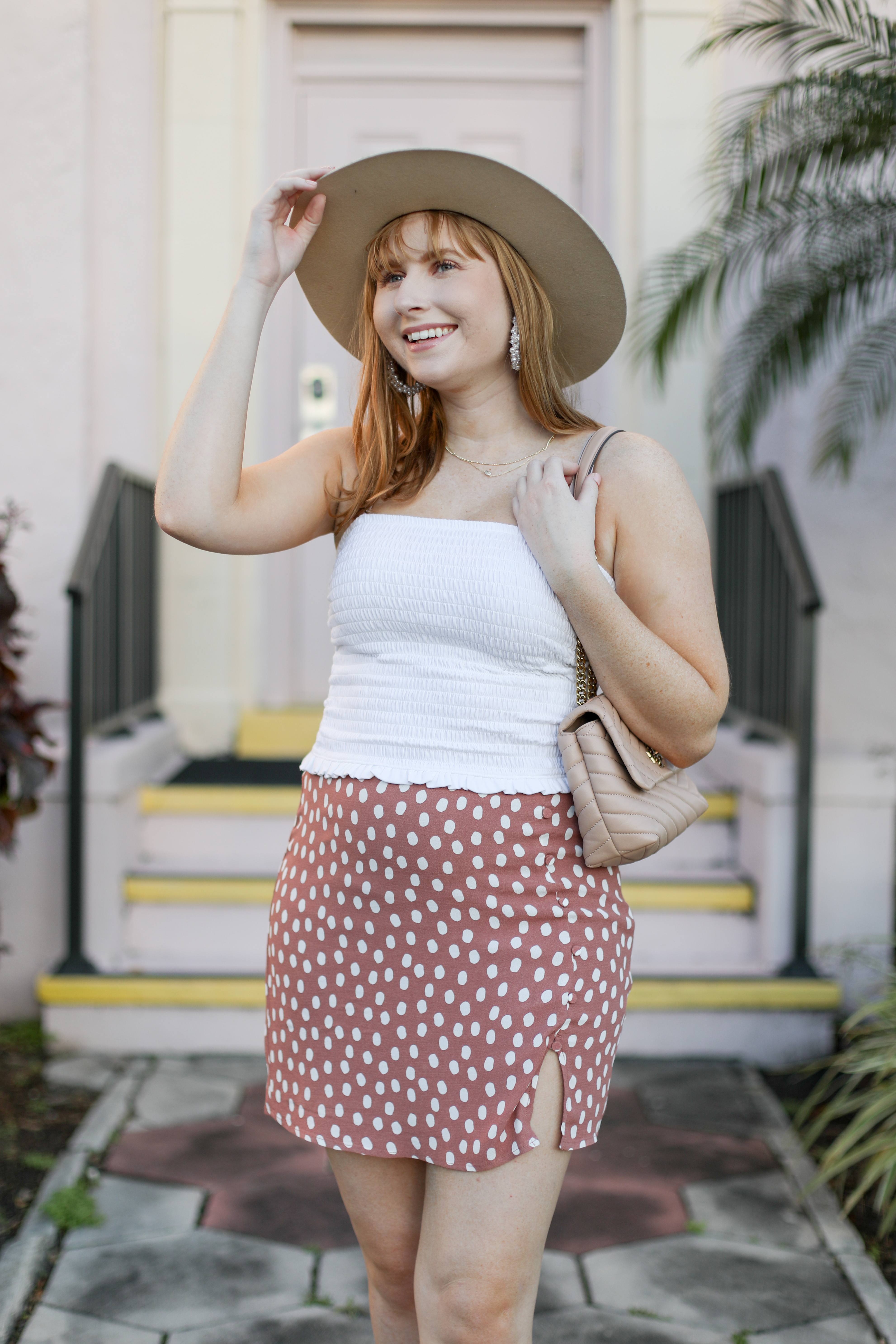 10 Vacation Outfit Ideas 2021 - Affordable by Amanda, Amanda Burrows wears a white camisole tank top, pink polka dot mini skirt, beige hat, and light pink bag on her shoulder.