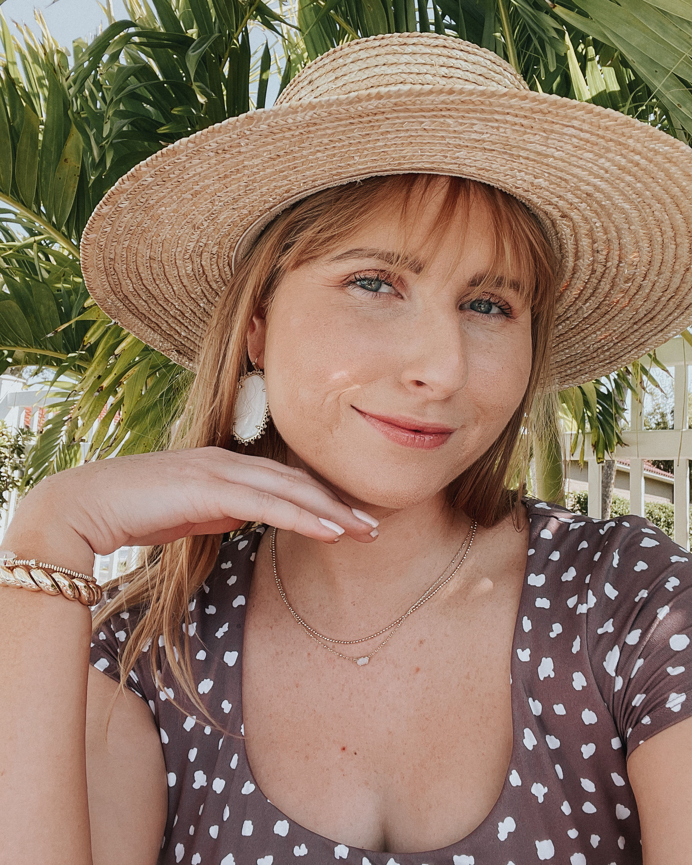 Amanda Burrows of Affordable by Amanda shares her May favorites, including the Beaded Danielle Gold Drop earrings from Kendra Scott. She is wearing a beige sun hat and charcoal gray polka dot bathing suit top.