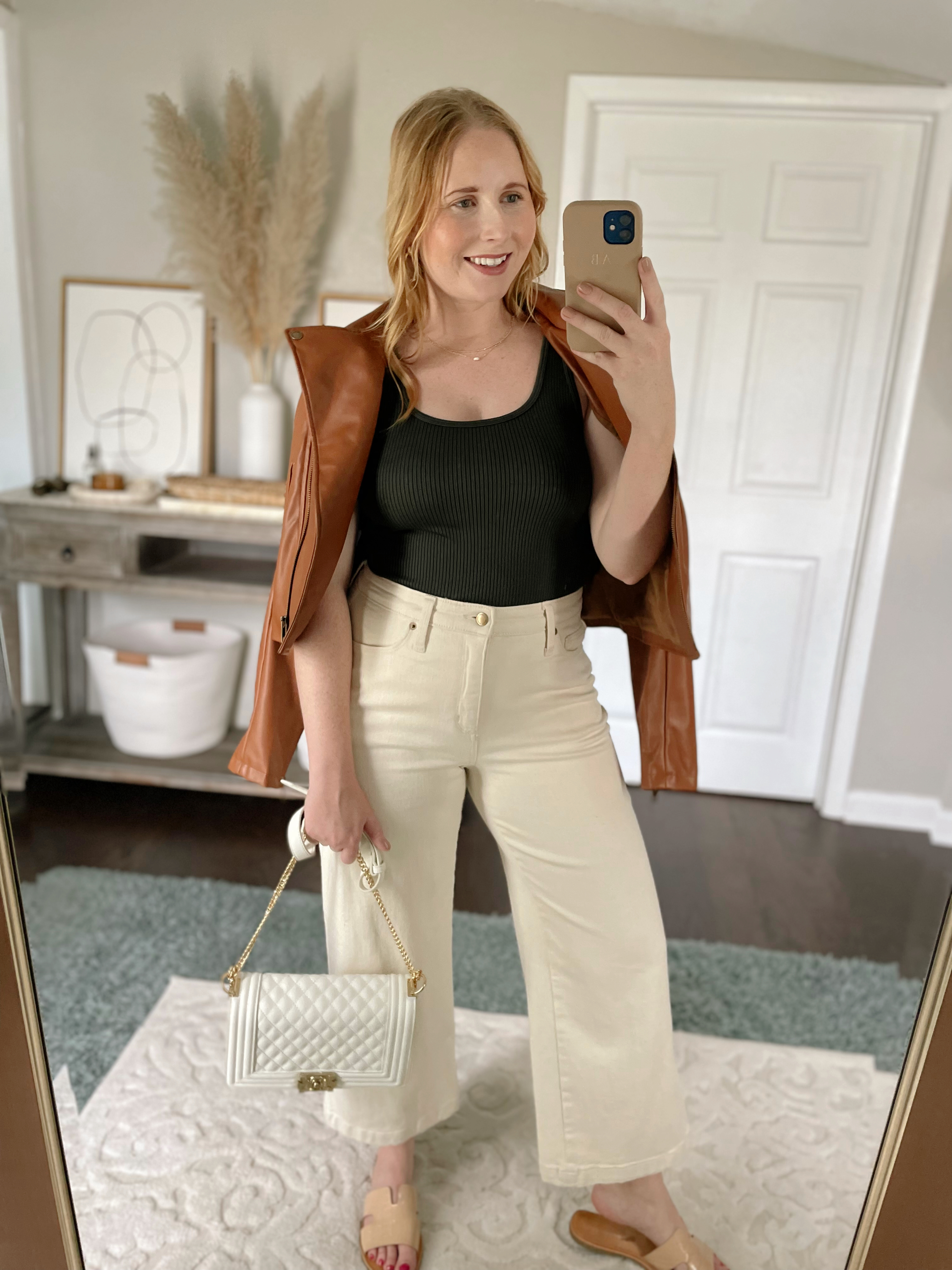 Affordable by Amanda wears a green ribbed tank top, brown faux leather moto jacket, cream wide leg pants while holding a white quilted bag