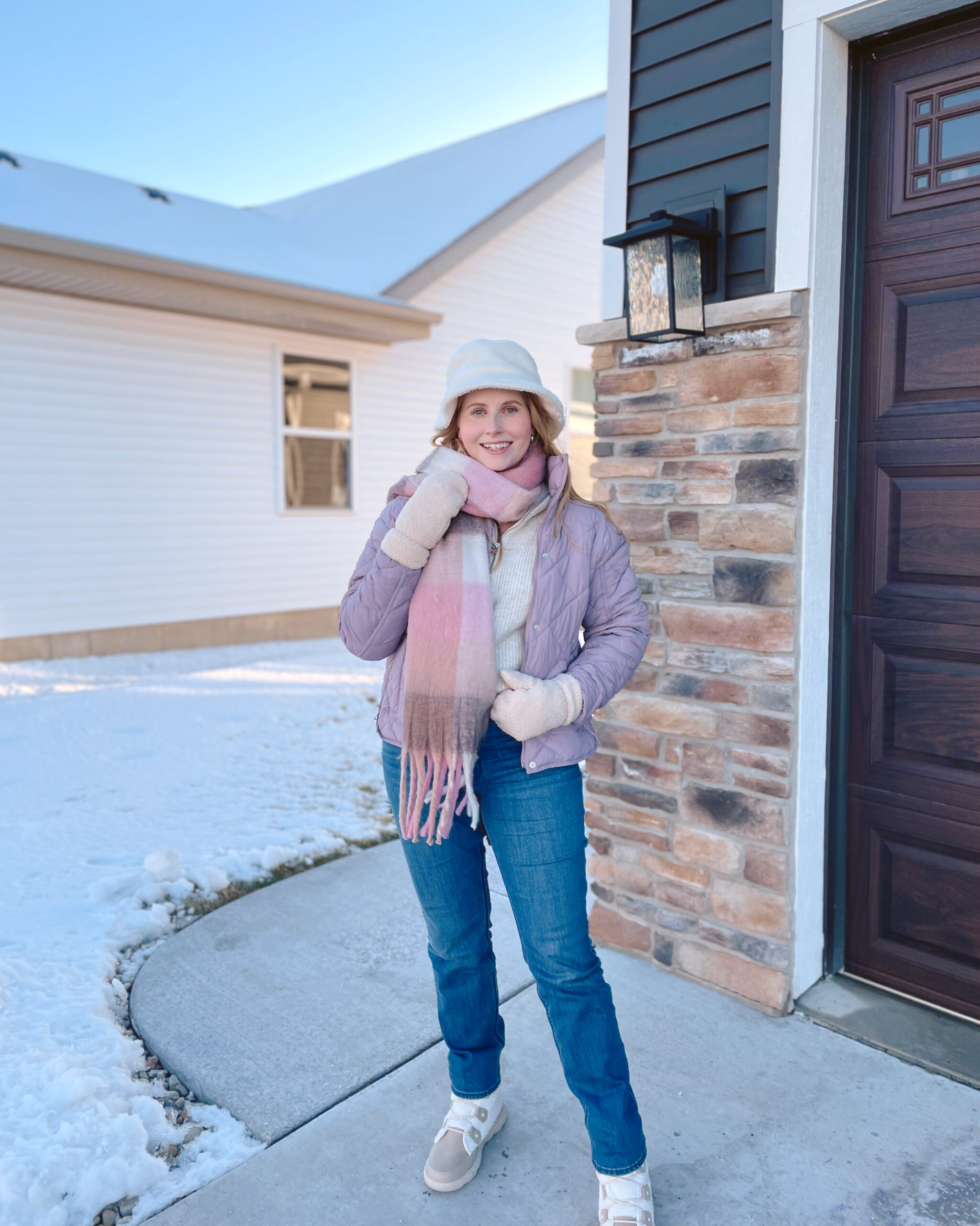 Affordable by Amanda wears a purple puffer jacket, white sherpa bucket hat, plaid scarf, jeans, and sorel winter boots